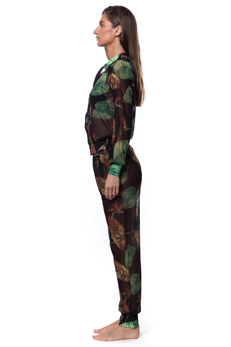 Side view of woman wearing Bella Paradise tropical print mesh bomber with matching pants in dark green and brown